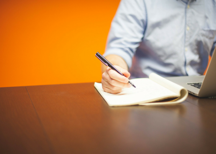 Image of a person working on their laptop and writing something on a notepad